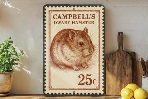 A stamp-like sign with a picture of a hamster and the text "CAMPBELL'S DWARF HAMSTER" on it, along with the price "25c". The sign is placed on a wooden surface, with a potted plant, a wooden cutting board, and some lemons nearby.