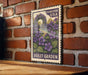 A vintage-style postage stamp featuring a purple garden scene with purple flowers and green leaves, mounted on a brick wall.
