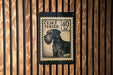 a black and white postage stamp with a dog illustration on it, mounted on a wooden wall.