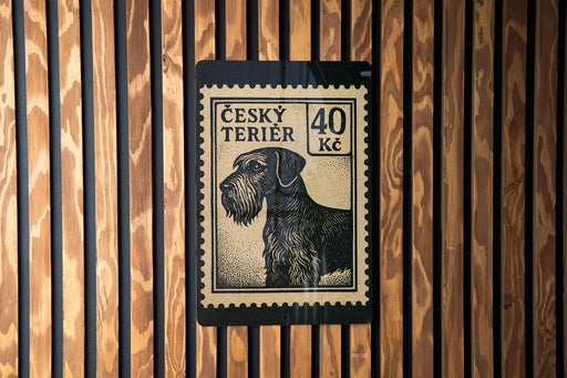 a black and white postage stamp with a dog illustration on it, mounted on a wooden wall.