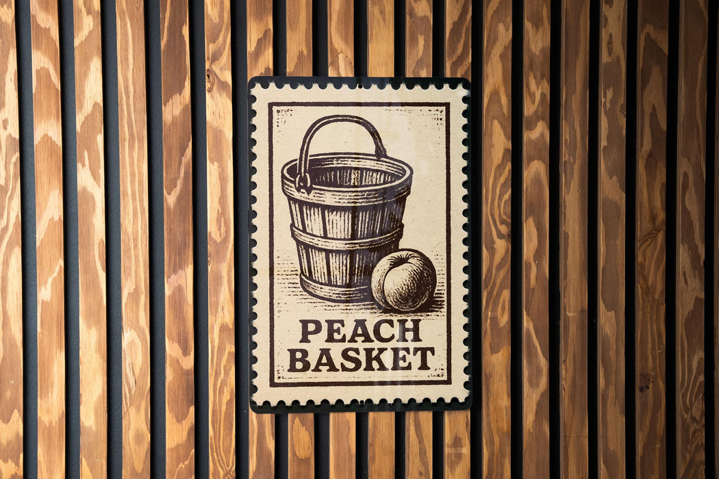 A wooden wall with a metal sign featuring an illustration of a peach basket and the text "PEACH BASKET" printed on it.