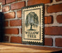 a sign with the text "WILLOW TREES" and a graphic of a willow tree. The sign is mounted on a brick wall, and there is a wooden table below it.