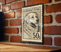 A black and white postage stamp featuring a dog's portrait is displayed on a brick wall.
