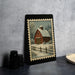 A framed painting of a red barn with a snowy landscape in the background is displayed on a table.