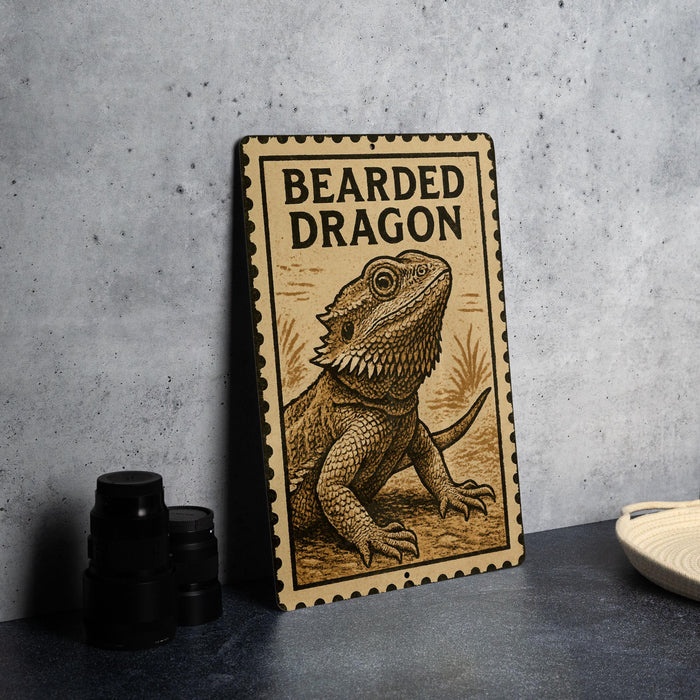 A metal sign with a bearded dragon illustration on it, placed on a table next to some black camera lenses.