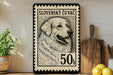 A framed stamp depicting a dog, with the text "SLOVENSKÝ CUVĚCĚ" and "50h" printed on it, is displayed on a shelf next to a wooden cutting board and some kitchen utensils.