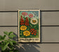 A colorful postage stamp featuring a floral design is displayed on a wall, with a plant to the left.