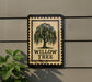 a sign with the text "WILLOW TREES" and a tree illustration, mounted on a wall next to a plant.