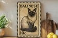 A framed illustration of a Siamese cat on a postage stamp, with the word "BALINESE" written above it. The cat is sitting on a wooden surface, and there are some potted plants and kitchen utensils visible in the background.
