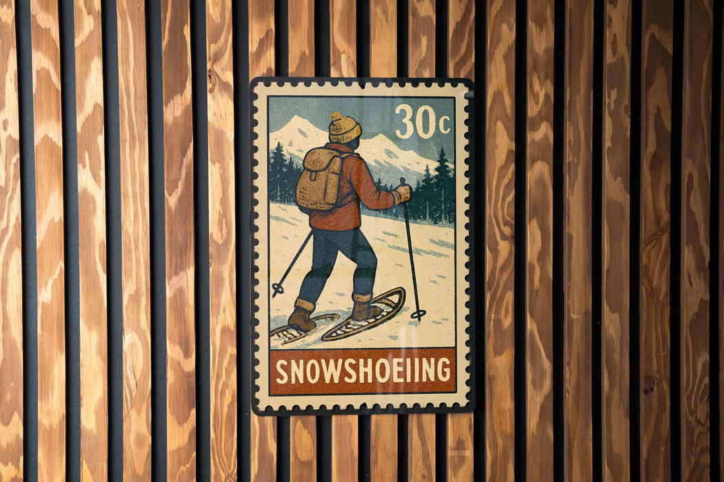 A vintage-style postage stamp depicting a person skiing on snowshoes, with the word "SNOWSHOEOING" written below the illustration.