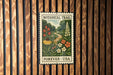 A vintage-style postage stamp featuring a lush, colorful garden scene with flowers and a winding path, mounted on a wooden wall.