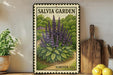 A framed poster of purple flowers is displayed on a shelf, with a wooden cutting board and a potted plant to the left.