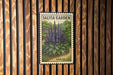 A framed image of purple flowers is displayed on a wooden wall, with a vintage-style postage stamp in the center.