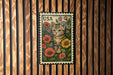 A vintage-style postage stamp featuring a cat surrounded by colorful flowers, placed on a wooden wall.