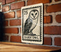 A metal sign featuring a barn owl illustration is mounted on a brick wall.