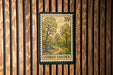 A postage stamp featuring a scenic landscape with a winding path and trees, mounted on a wooden wall.