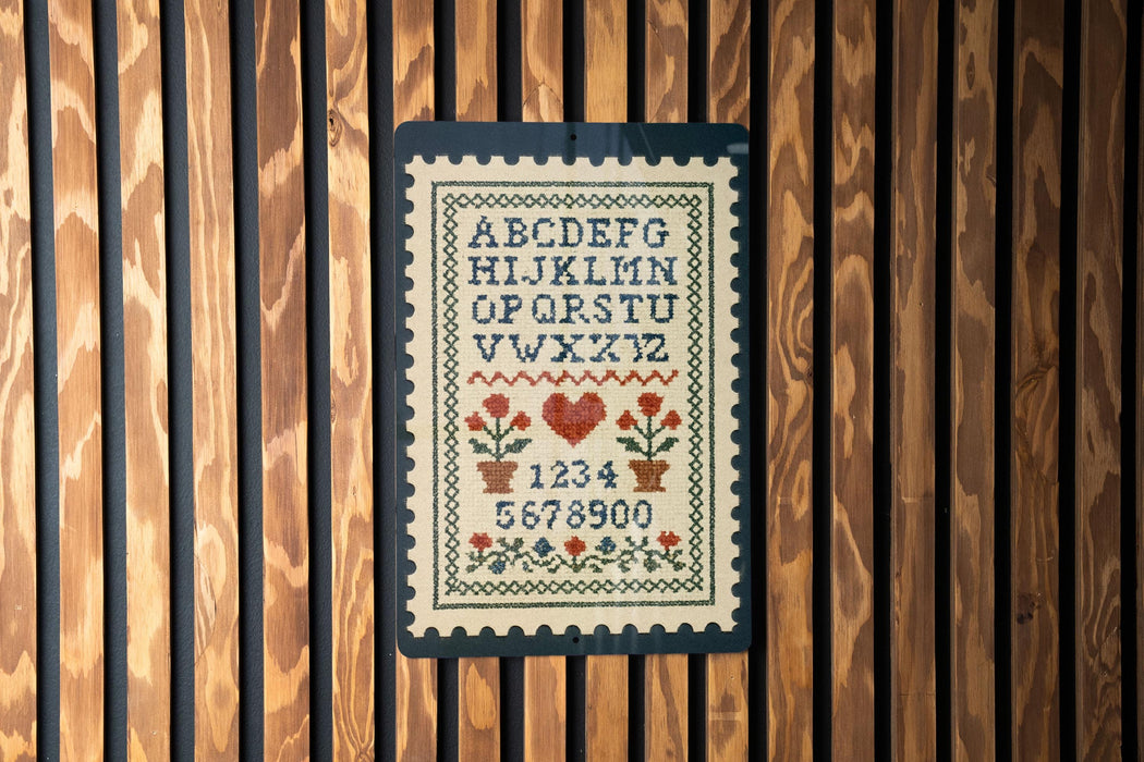 a cross-stitch pattern with the alphabet and numbers displayed on a wooden panel.
