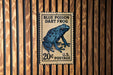 A blue poison dart frog postage stamp is displayed on a wooden wall.