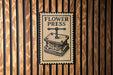 A sign for a "flower press" is displayed on a wooden wall.