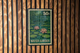 A green and white postage stamp with a water garden illustration, mounted on a wooden wall.