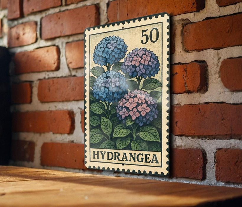 A vintage-style metal stamp with a floral design is displayed on a brick wall, featuring a close-up of three blue hydrangea flowers.