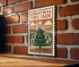 A Christmas tree farm sign is displayed on a brick wall, featuring a large illustration of a Christmas tree and a scenic landscape.