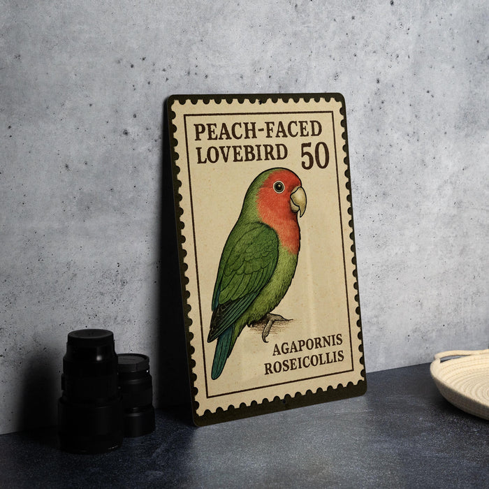 A metal stamp featuring a colorful illustration of a peach-faced lovebird, with the text "Peach-faced Lovebird 50" and "Agapornis Roseicolis".