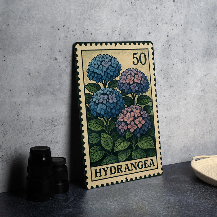 A metal stamp featuring a floral design with blue and pink hydrangea flowers, placed on a table next to some black camera lenses.