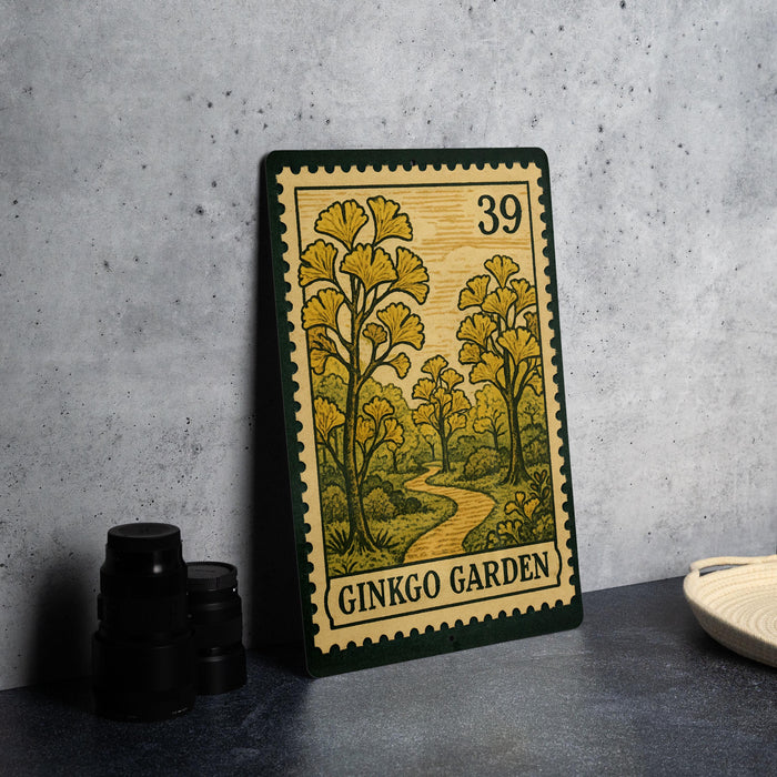 A framed postage stamp depicting a scenic landscape with trees and a winding path, placed on a table next to some black camera lenses.