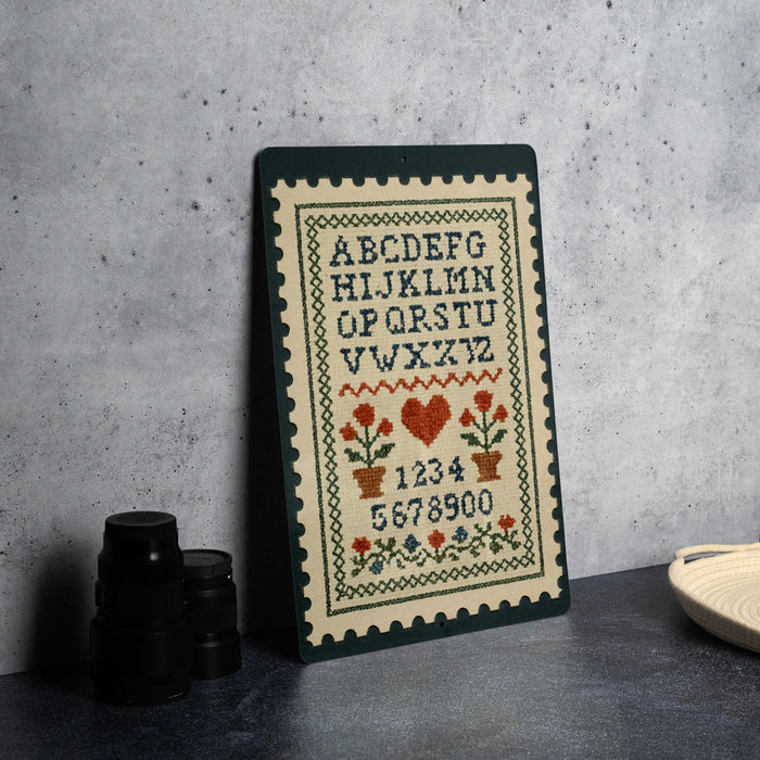 a cross-stitch embroidery of the alphabet on a wooden frame, placed on a table next to some black camera lenses.