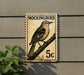 A postage stamp-like sign featuring a bird perched on a branch, mounted on a wall.