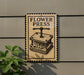 A sign for a flower press is displayed on a wall, with a plant visible to the left.