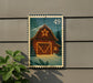 A wooden barn with a star decoration is depicted on a postage stamp, which is affixed to a wall.