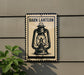 A metal sign with a lantern illustration is mounted on a wall, next to a plant.