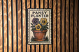 A metal sign with a potted plant and the text "PANSY PLANTER" is displayed on a wooden wall.
