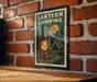 A lantern camping sign is displayed on a brick wall, featuring an illustration of a lantern and a tent in a wooded area.
