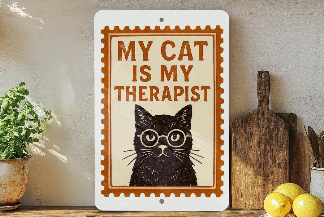 a sign with a black cat wearing glasses and the text "MY CAT IS MY THERAPIST" on it, placed on a wooden surface next to a potted plant and a cutting board.