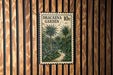 A postage stamp with a tropical garden scene is displayed on a wooden wall.