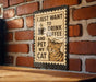 A sign with a cat and the text "I JUST WANT TO DRINK COFFEE AND PET MY CAT" is displayed on a brick wall.
