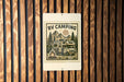 a sign with a camping scene, including a camper van, a campfire, and mountains in the background.