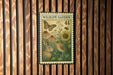 A wildlife garden stamp with a rabbit, bird, and flowers is displayed on a wooden wall.