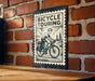 A bicycle touring sign is mounted on a brick wall, featuring an illustration of a person riding a bicycle.