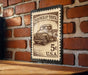A vintage-style stamp depicting an old pickup truck, mounted on a brick wall.