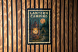 A lantern camping poster is displayed on a wooden wall, featuring a lantern, tent, and trees in a nighttime setting.