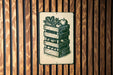 A metal sign with a black and white illustration of a wooden crate filled with various vegetables, such as corn, apples, and carrots, mounted on a wooden wall.