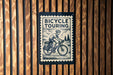 A bicycle touring sign is displayed on a wooden wall.