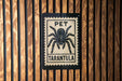 A sign with a black and white illustration of a tarantula, mounted on a wooden wall.