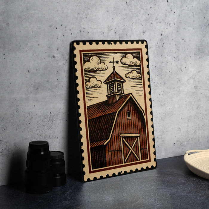 A framed illustration of a barn with a cross on top, depicting a rural scene, is displayed on a table next to some black camera lenses.