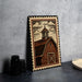 A framed illustration of a barn with a cross on top, depicting a rural scene, is displayed on a table next to some black camera lenses.