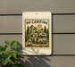 a sign with a camping scene, including a camper van, trees, and a campfire, mounted on a wall.